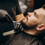 Handsome man cutting beard at a barber shop salon